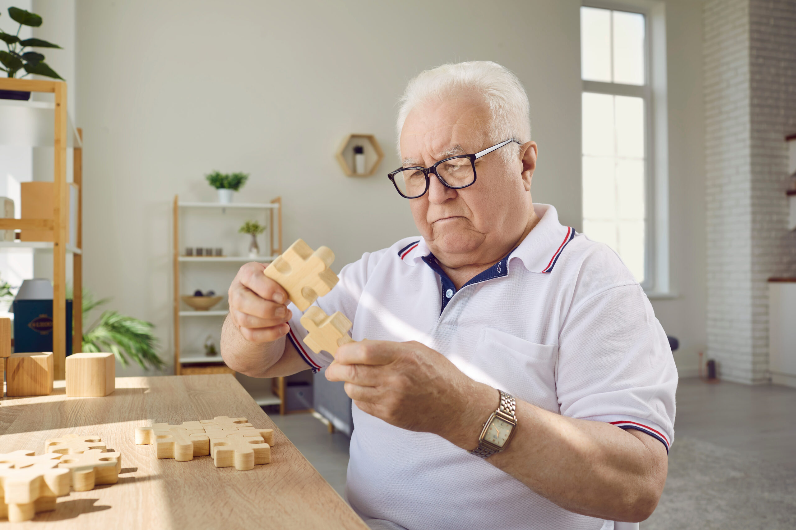 Concentrated senior man in nursing home putting wooden puzzle to prevent alzheimer.